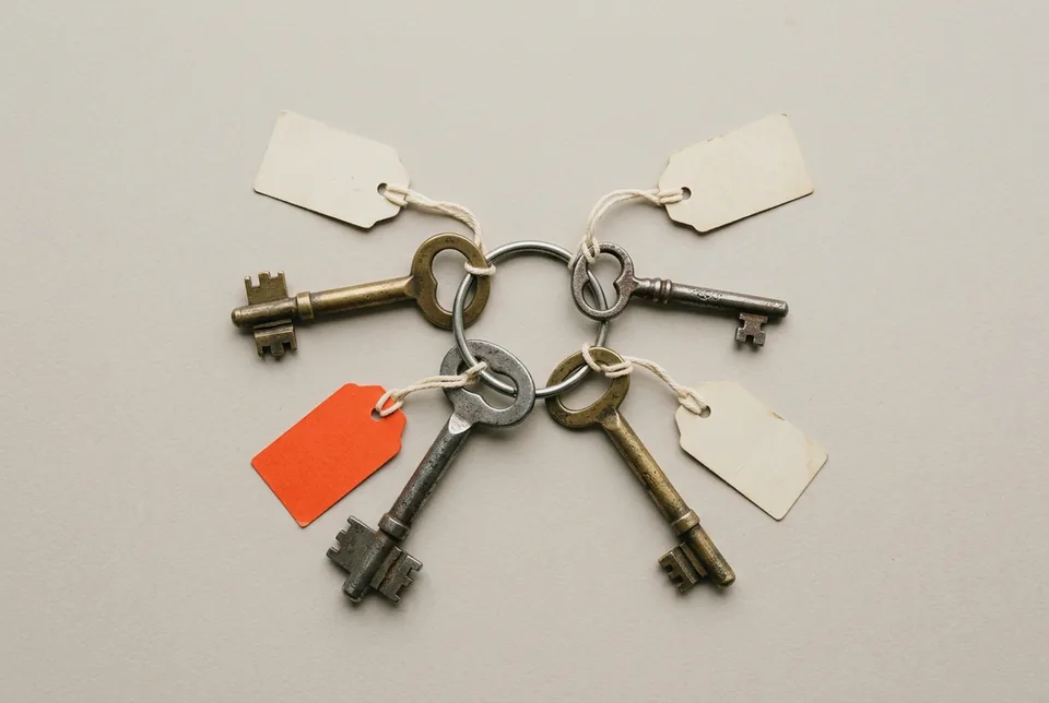 A ring of four old keys, each with a blank paper tag, one tag orange-red