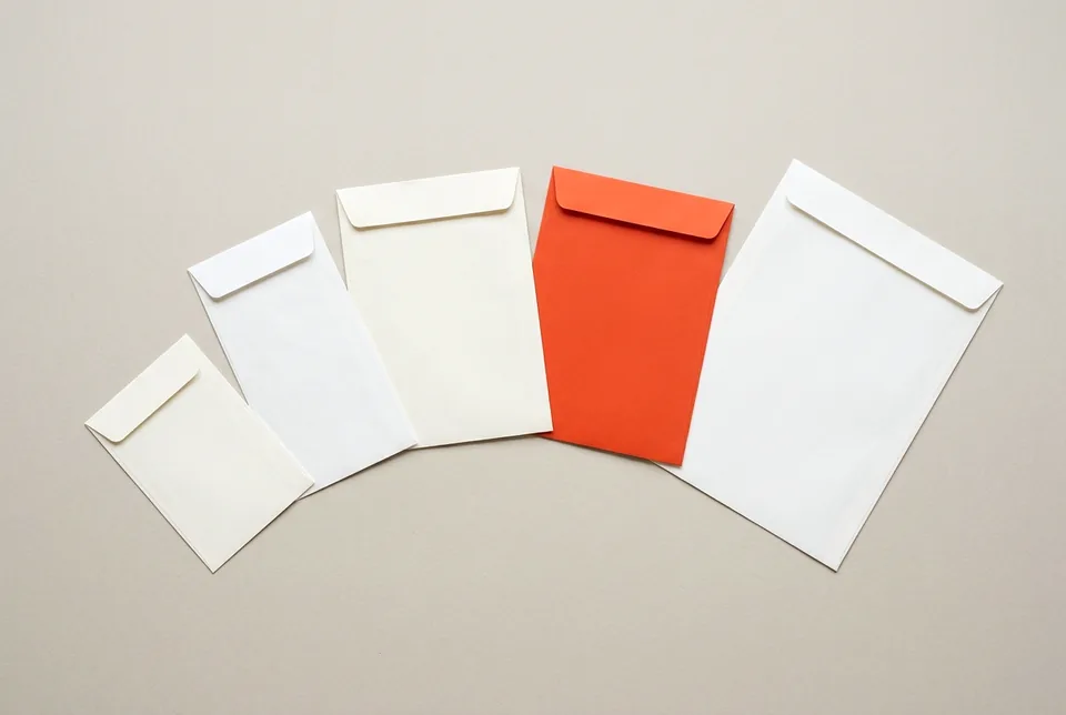 Five blank envelopes of different sizes fanned out, one orange-red