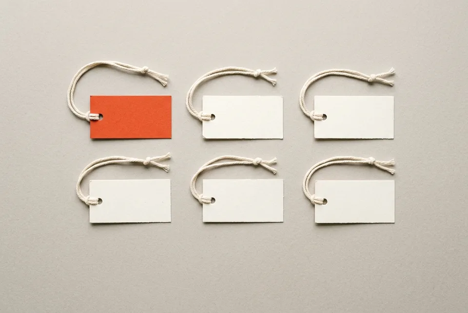 Six blank paper tags on strings laid out in two rows, one orange-red
