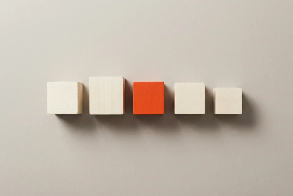 Five wooden blocks of different heights in a row, one orange-red