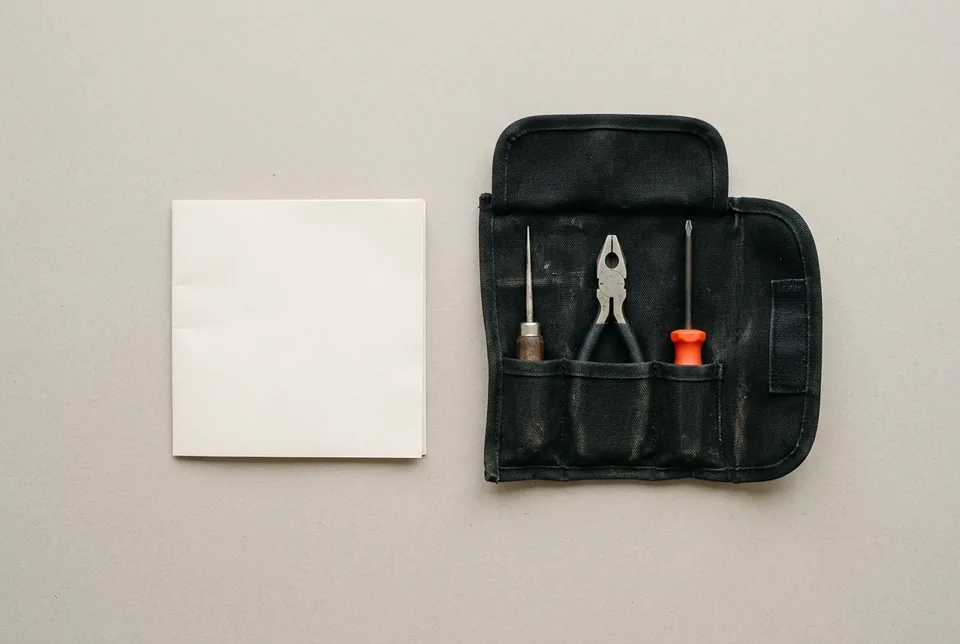 A folded blank sheet beside an open tool roll of hand tools, one with an orange-red handle