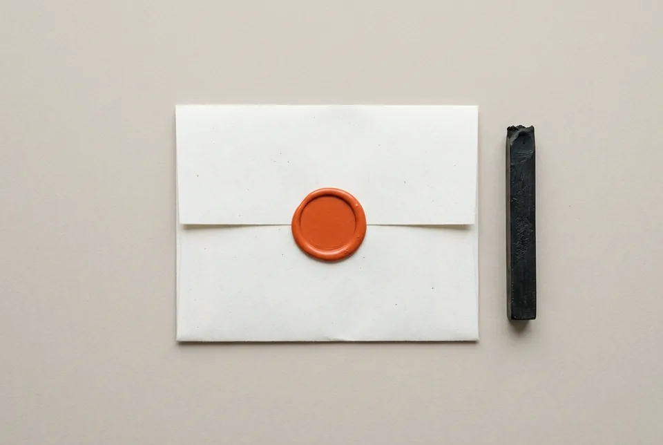 A folded sheet closed with a plain orange-red wax seal, beside a stick of sealing wax